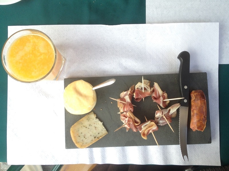 Mesa com suco e quatro variedades de embutidos portugueses, sendo dois tipos de queijos, um presunto e um salame