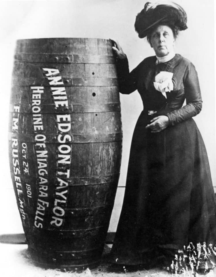 Annie Edson Taylor posa ao lado de seu barril em uma foto em preto e branco.
