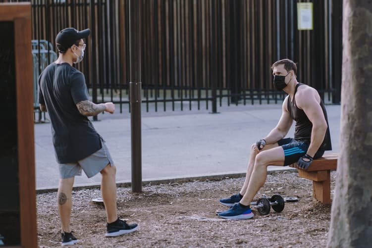 Dois jovens usam máscaras enquanto fazem esportes em um parque.